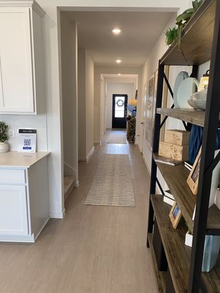 A modern hallway with light wood floors, built-in shelving, and sleek recessed lighting, leading to a welcoming front door.