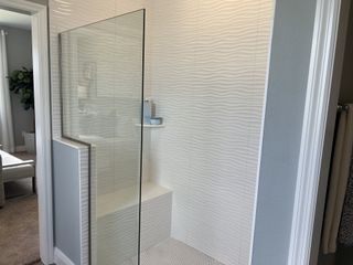 Model Home A contemporary shower with wave-patterned tiles, a glass partition, and minimalist design accents.