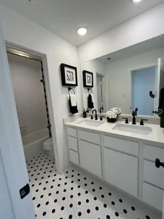 A chic bathroom featuring dual sinks, black hardware, and a black-and-white hex tile floor.