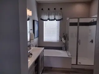 Model Home A modern bathroom featuring a glass shower, elegant fixtures, and natural light from a window with striped curtains.