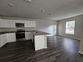 Spacious kitchen with white cabinetry, granite countertops, stainless steel appliances, and dark wood flooring.