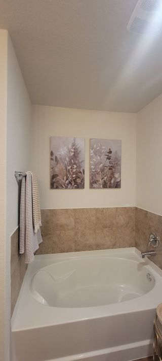 A relaxing bathroom featuring a large soaking tub with tile surround, neutral walls, and framed botanical artwork.