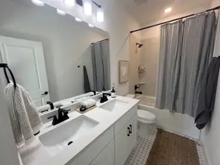 A stylish bathroom with a double vanity, sleek black fixtures, and a tiled shower in Solterra Texas by Cadence Homes (Mesquite, TX).