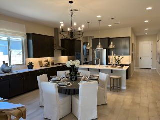 A modern kitchen with dark cabinetry, a central dining table, elegant lighting fixtures, and stainless steel appliances.