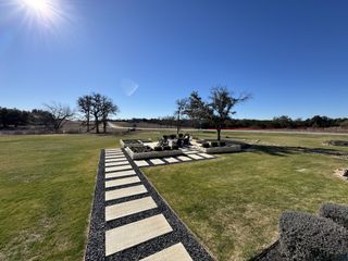 Model Home A spacious backyard with a scenic view, featuring a paved walkway and a landscaped firepit area in North Haven by GFO Home (Liberty Hill, TX).
