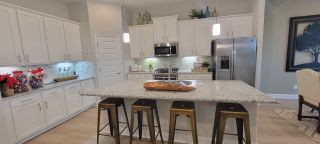 Model Home A modern kitchen featuring a spacious granite island, sleek white cabinetry, and stylish pendant lighting.