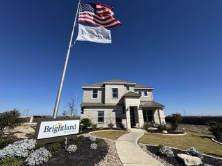 Street view A beautiful home with an American flag and a landscaped yard in Dauer Ranch by Brightland Homes (New Braunfels, TX).