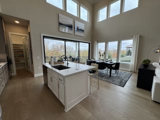 A modern open-concept kitchen and dining area with high ceilings, large windows, and wood floors creates a bright and airy space.