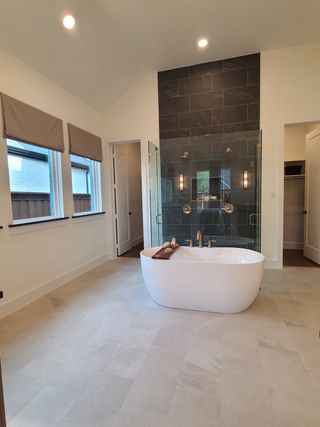 A luxurious bathroom with a sleek freestanding tub, glass-enclosed shower, and elegant dark tile accents.