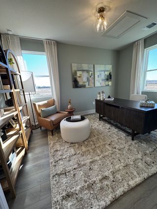 A cozy home office with modern decor, abstract art, a plush rug, and natural light from large windows.