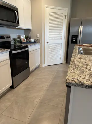 A modern kitchen with granite countertops, stainless steel appliances, and sleek white cabinets.