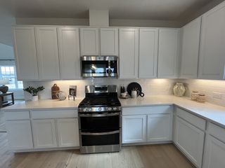 Model Home A sleek kitchen with white cabinetry, stainless steel appliances, and under-cabinet lighting.