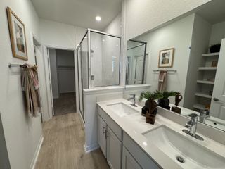 A sleek bathroom with dual sinks, framed art, a glass shower enclosure, and open shelving.