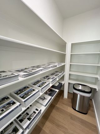 A sleek storage room with white shelves, showcasing organized photo books, hardwood floors, and a modern trash bin.