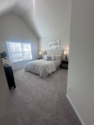Model Home A serene bedroom featuring a vaulted ceiling, cozy carpet, and elegant decor with soft lighting.