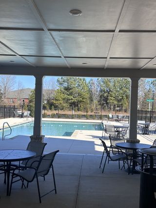 Community Amenities A covered patio area with tables overlooks a serene outdoor pool, surrounded by trees and a fenced perimeter.