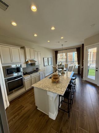 Model Home A bright kitchen with a large granite island, stainless steel appliances, and white cabinetry.