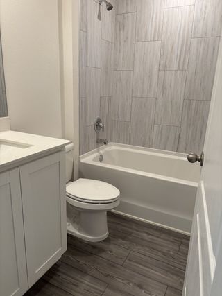 A modern bathroom with light wood tiles, a sleek bathtub, and a white vanity.