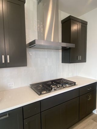 A modern kitchen with sleek dark cabinets, a stainless steel range hood, and elegant white countertops.