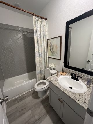 A cozy bathroom with a sleek granite-topped vanity, dark fixtures, and herringbone-tiled shower.