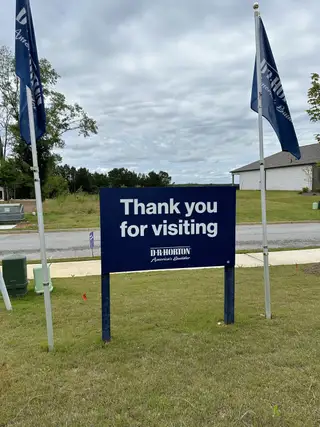 Visitor signage at Oaks at Cedar Grove by D.R. Horton, surrounded by greenery in Fairburn, GA.