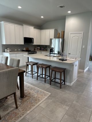Model Home A modern kitchen with white cabinetry, stainless steel appliances, and a cozy dining area with a stylish rug and bar stools.