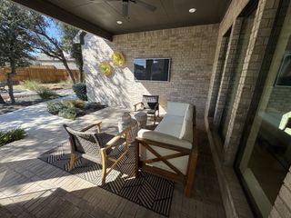 A cozy covered patio with elegant wicker furniture, brick walls, and a television, perfect for relaxation.