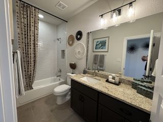 A modern bathroom features a granite countertop, stylish lighting, and a tub with patterned shower curtain.