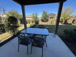 A cozy patio with a glass table, chairs, and a view of a lush, landscaped backyard.