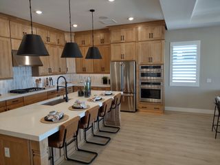 A modern kitchen with sleek pendant lights, wooden cabinetry, stainless steel appliances, and a spacious island with seating.