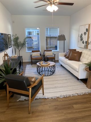 Model Home A bright living room with a white sofa, leather accent chairs, a round coffee table, and natural light from two windows.