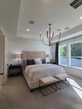 A cozy bedroom with a plush tufted bed, elegant chandelier, and ample natural light from large windows.