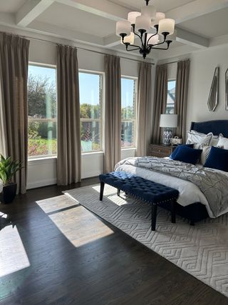 Elegant bedroom with large windows, wood floors, a plush navy bench, and chic lighting.