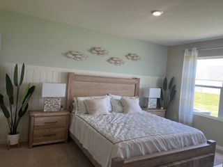A cozy bedroom with a wooden bed frame, green accents, decorative wall art, and large windows for natural light.