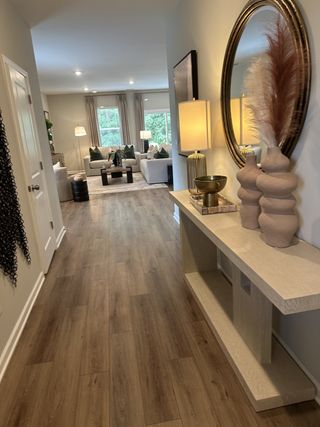 A chic hallway with wood floors, elegant decor, and a bright living area in the distance, showcasing modern interior design.
