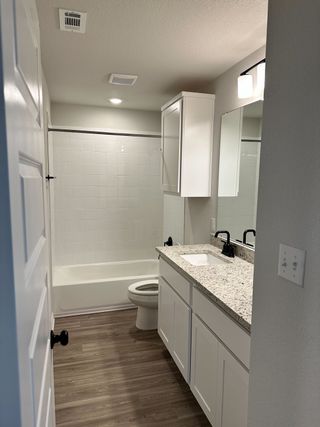 Model Home A modern bathroom with sleek white cabinetry, a granite countertop, and wood-style flooring.