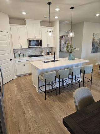 A modern kitchen with white cabinets, a spacious island, pendant lighting, and wood flooring.