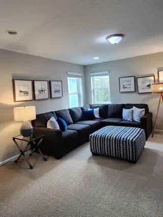 A cozy living room with a dark sectional sofa, striped ottoman, and soft lighting, creating a warm and inviting atmosphere.