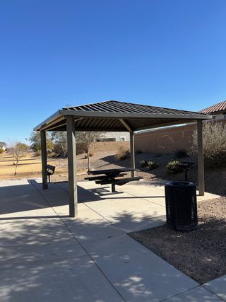 A community area with a metal pavilion, picnic table, and trash bin in Tortosa by KB Home (Maricopa, AZ).