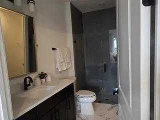 A modern bathroom with a glass-enclosed shower, marble-look floors, and a chic black vanity with gold accents.