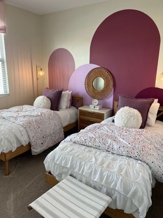 A cozy bedroom with twin beds, vibrant arched wall accents, and soft, textured pillows for a playful feel.