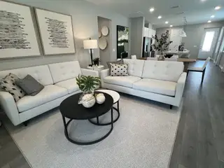 A modern living room with sleek white sofas, abstract art, and light hardwood flooring leading to an open dining area.