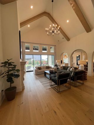 A spacious living room with vaulted ceilings, exposed beams, and a grand chandelier, featuring cozy seating and natural light.