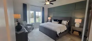 A cozy bedroom featuring a plush gray bed, stylish armchair, and ample natural light from large windows.