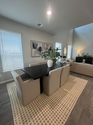A modern dining area with a sleek black table, beige chairs, abstract artwork, and soft natural lighting.