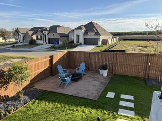A fenced backyard with a gravel seating area, Adirondack chairs, and green landscaping in The Colony 45 by David Weekley Homes (Bastrop, TX).