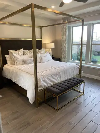 Model Home Luxurious bedroom featuring a king-size canopy bed, elegant gray bench, and large windows for abundant natural light.