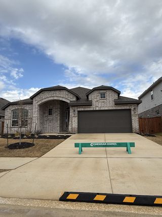 A beautiful brick home with a dark garage in Lariat by Chesmar Homes, featuring a spacious front yard (Liberty Hill, TX).