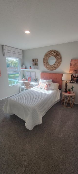 A cozy bedroom featuring a stylish coral headboard, soft carpeting, and a sunlit desk area by the window.
