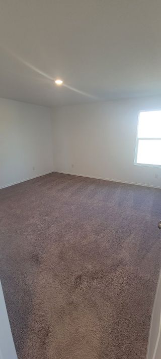 A spacious room with soft carpeting, neutral walls, and ample natural light from a single window.